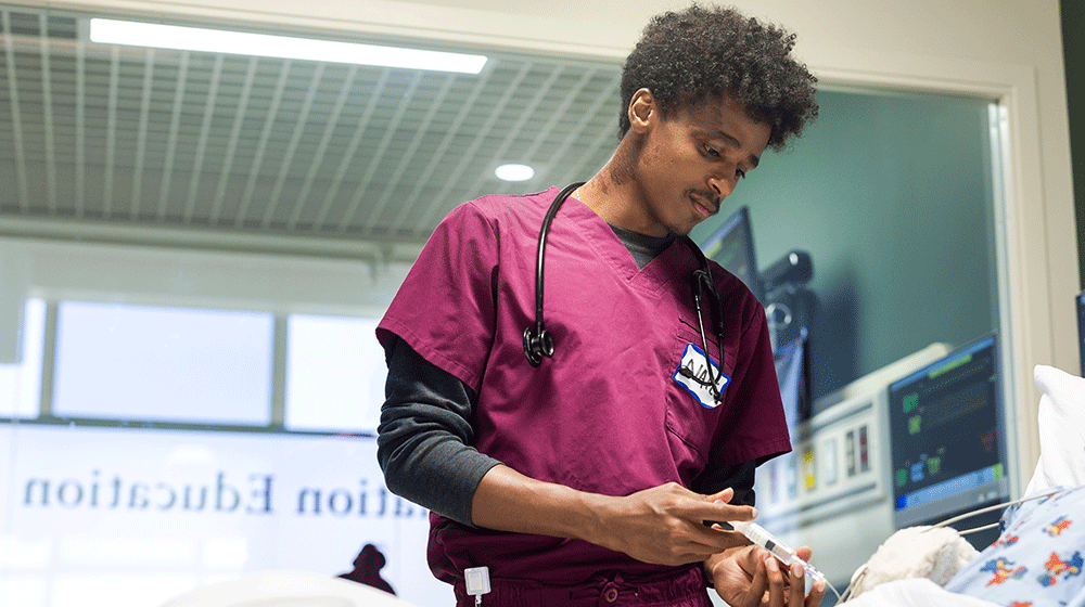 A student looks down at a manikin in the simulation lab at the Lake Shore Campus