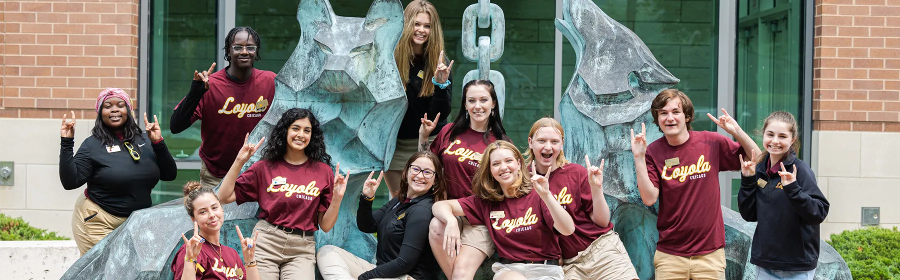 A group of students pose around a large statue of two wolves and a kettle that represents the generosity of the Ignatius family.
