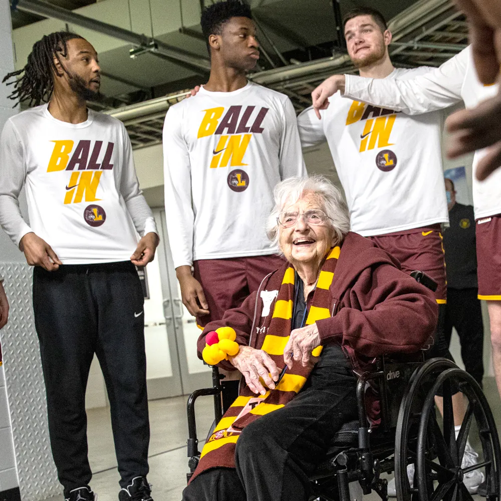 Sister Jean, sitting in her wheelchair, with three standing basketball players behind her.