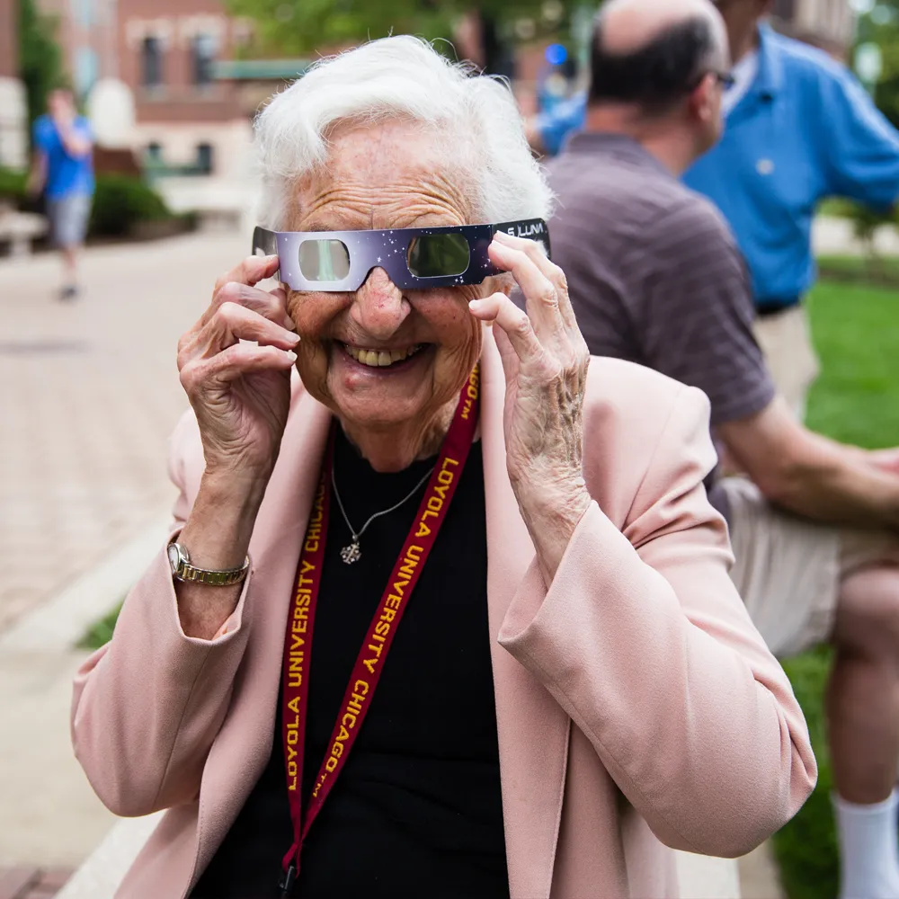 Sister Jean holds a pair of protective glasses to her eyes to view the eclipse.