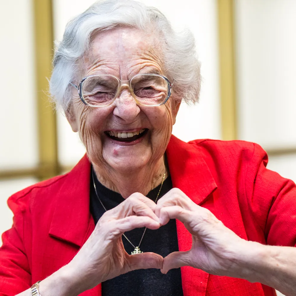 Sister Jean smiles as she makes a heart shape with her hands.