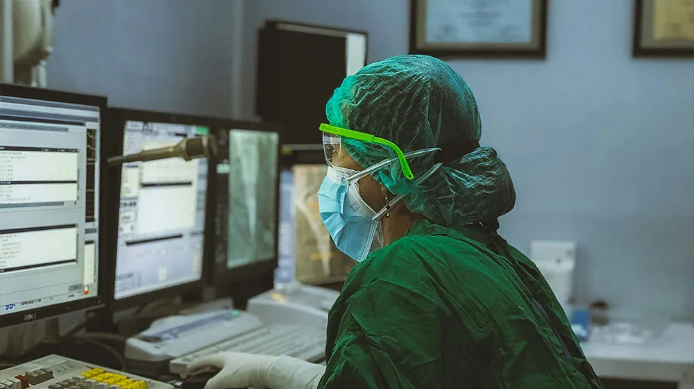 Masked doctor seated and working at a lab computer