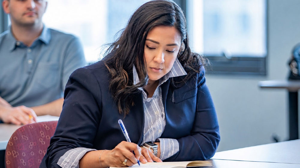 Woman seated in a classroom writing in her notebook Woman seated in a classroom writing in her notebook