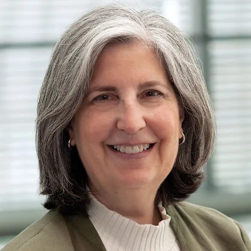 A woman in a green suit smiles while facing the camera against a grey background.