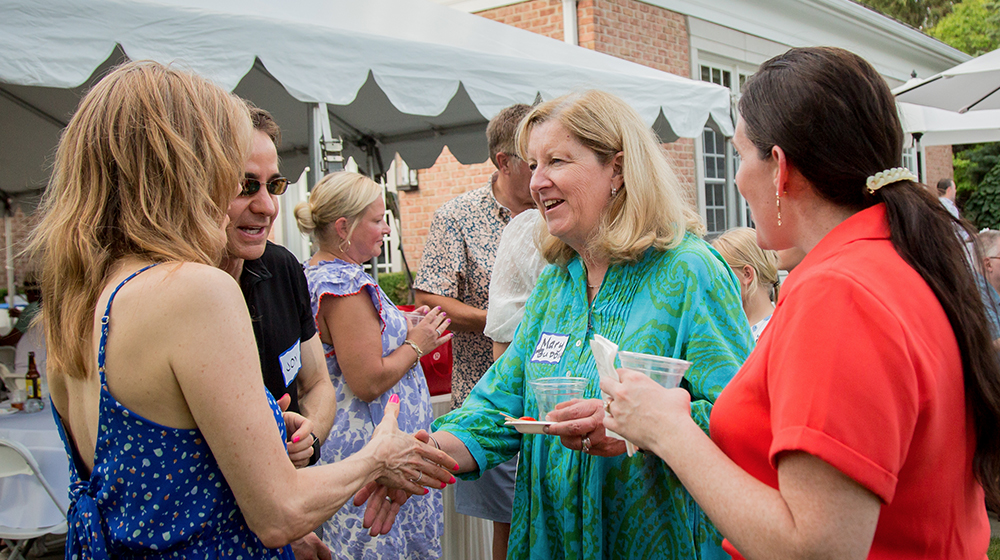 Three women and one man are talking in a group at a event wearing casual attire and name tags.