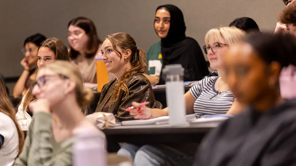 A group of students smile as they listen to the professor speak.