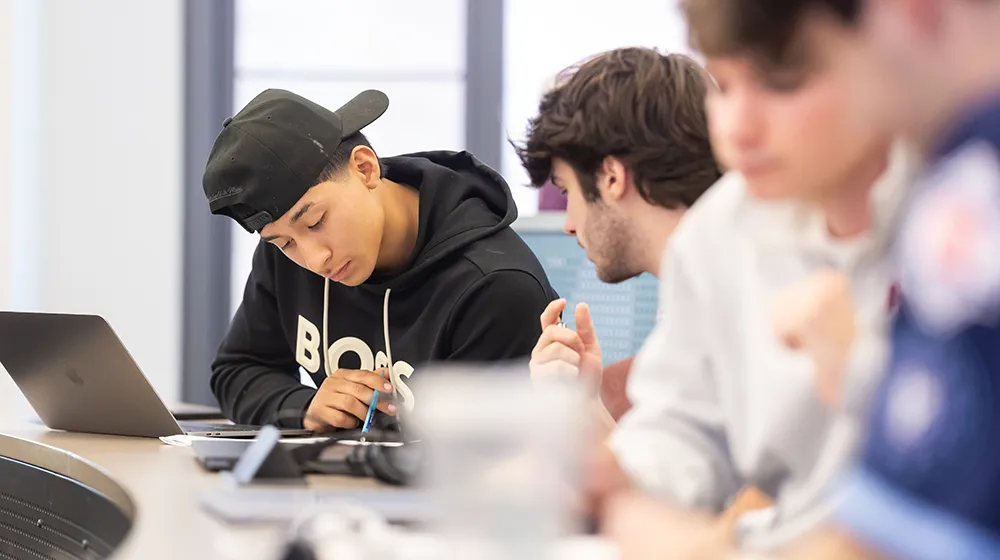 Students in Irem Sengal Orgut's class review work together. One student wears a black hoodie and a backward facing black baseball cap, the other wears a light shirt.