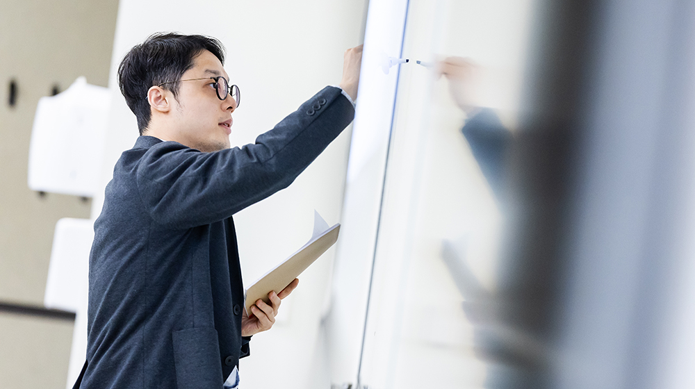 Yuxiao Rain Luo holds a notebook and writes on a whiteboard in a classroom.