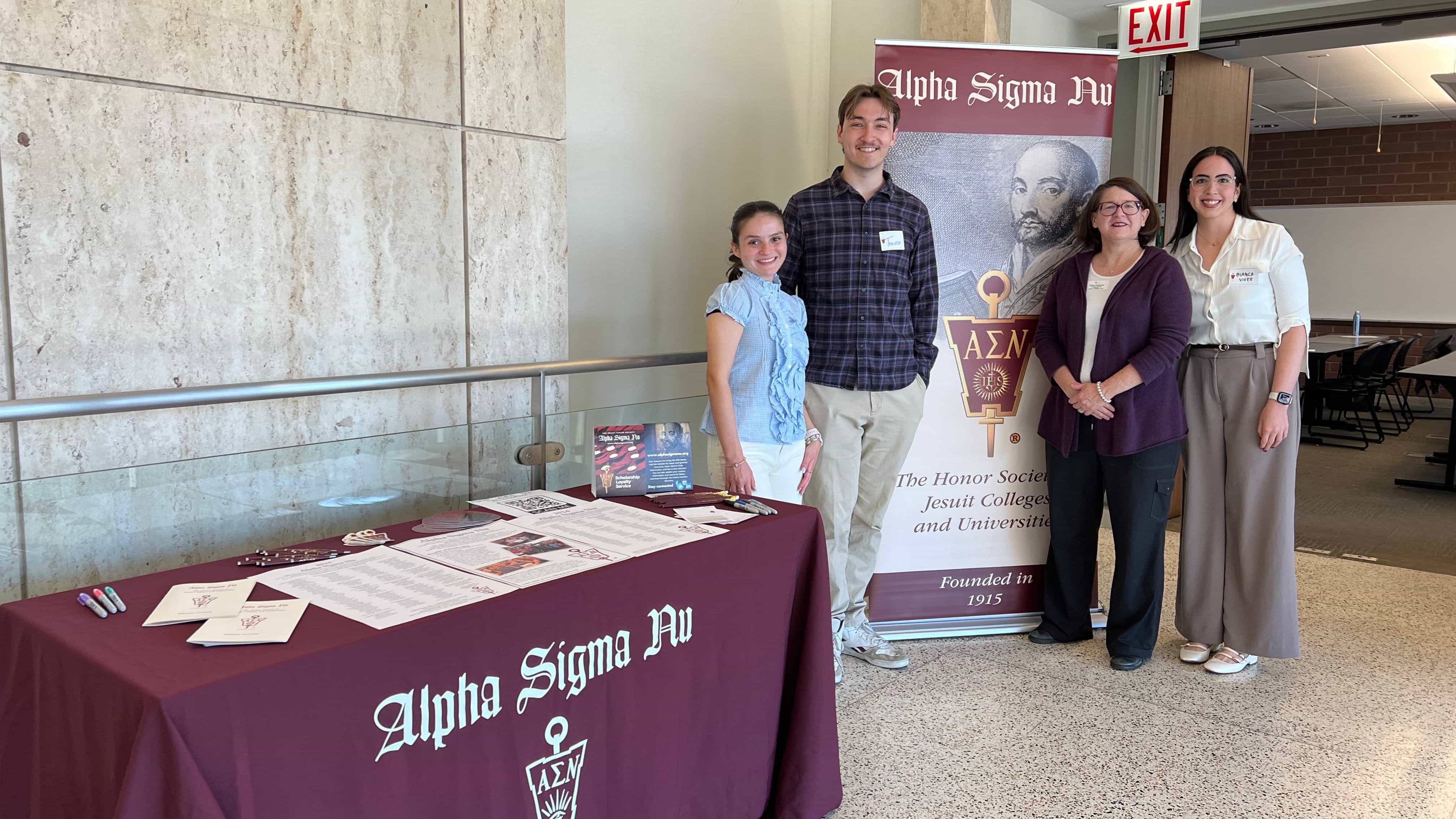 Two ASN chapter officers and two alumni members pose in front of ASN banner and table with ASN materials.