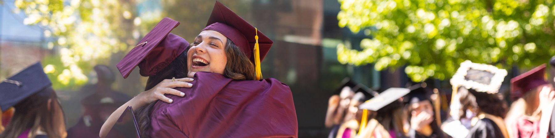 Студентка Университета Лойола в Чикаго обнимает и улыбается вне здания, празднуя выпуск в мае