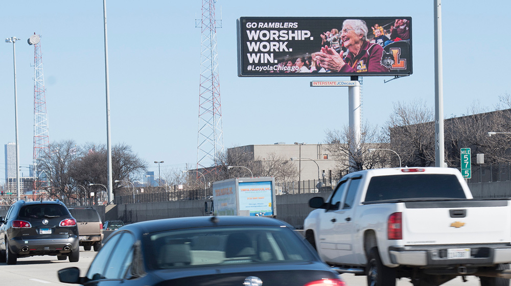 Cars drive along the highway beneath a large Loyola Chicago billboard promoting the team with bold text and celebratory imagery.