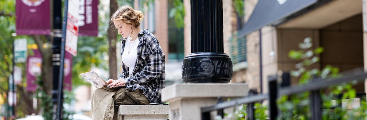 A student outside looking at their laptop