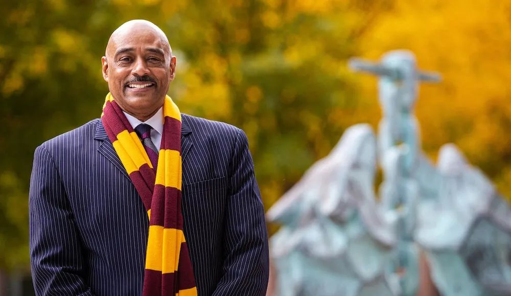 Keith Champagne wears a Loyola maroon and gold scarf standing in front of fall leaves and the Los Lobos statue on Lake Shore Campus.