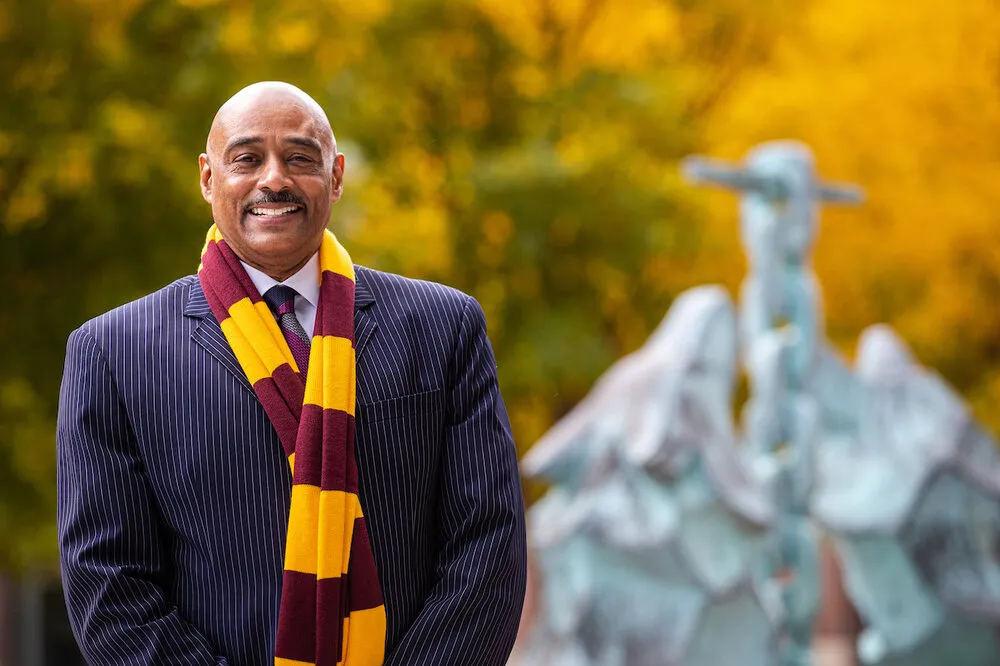 Keith Champagne wears a Loyola maroon and gold scarf standing in front of fall leaves and the Los Lobos statue on Lake Shore Campus.
