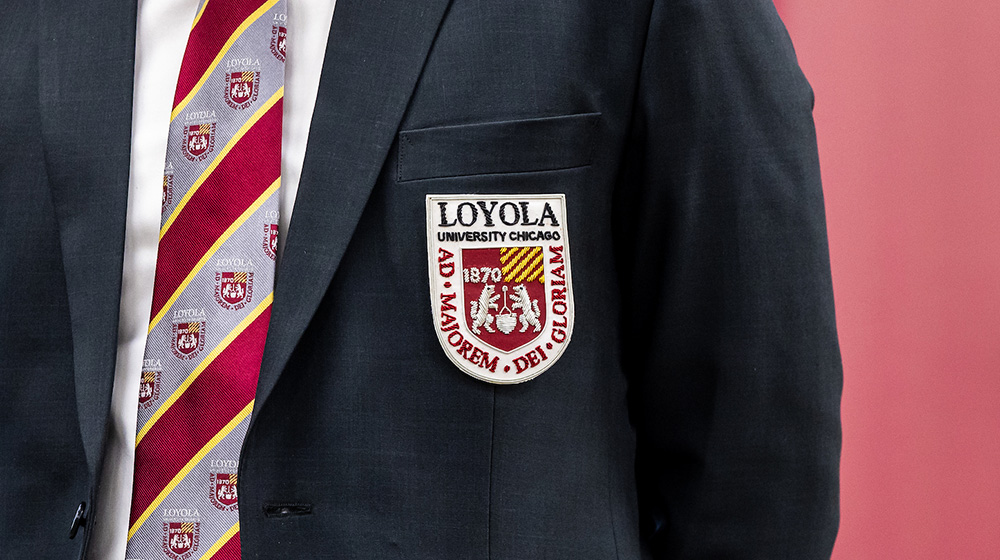 A close-up of a student wearing a suit with the Loyola seal embroidered on the breast and a Loyola-branded tie.