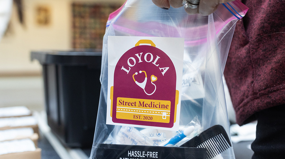 A volunteer holds a clear plastic bag filled with supplies and a sticker that says 