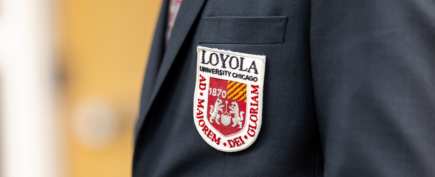 A close-up of a sportscoat breast and lapel with an embroidered patch of the Loyola University Chicago seal.
