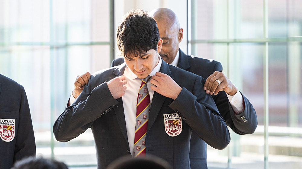 Dr. Keith Champagne helps a student put on the Rambler Brotherhood Project sportscoat during the induction ceremony.