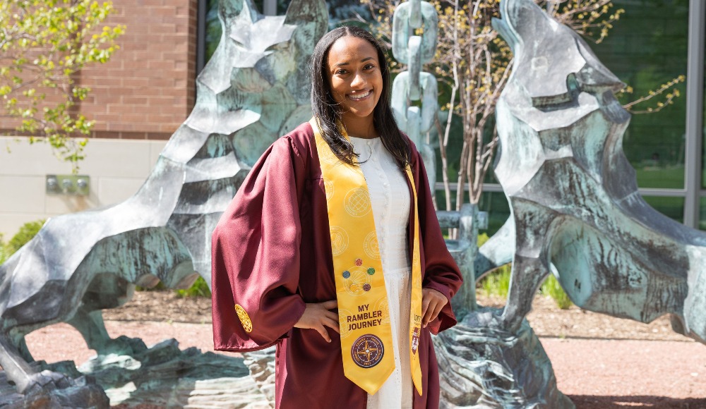 A student wearing graduation regalia poses in front of the Los Lobos statue on Lake Shore Campus.