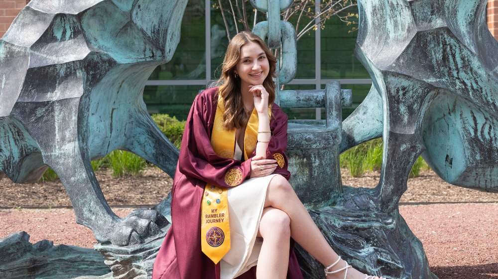 A student poses for a photo wearing the Rambler Journey pins and stole over their graduation regalia. A student poses for a photo wearing the Rambler Journey pins and stole over their graduation regalia.