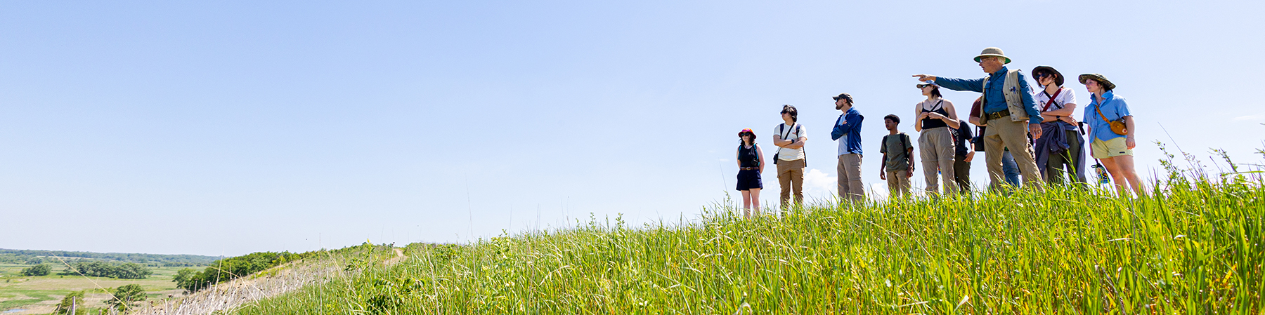 A group of students with faculty standing on a hill with someone pointing