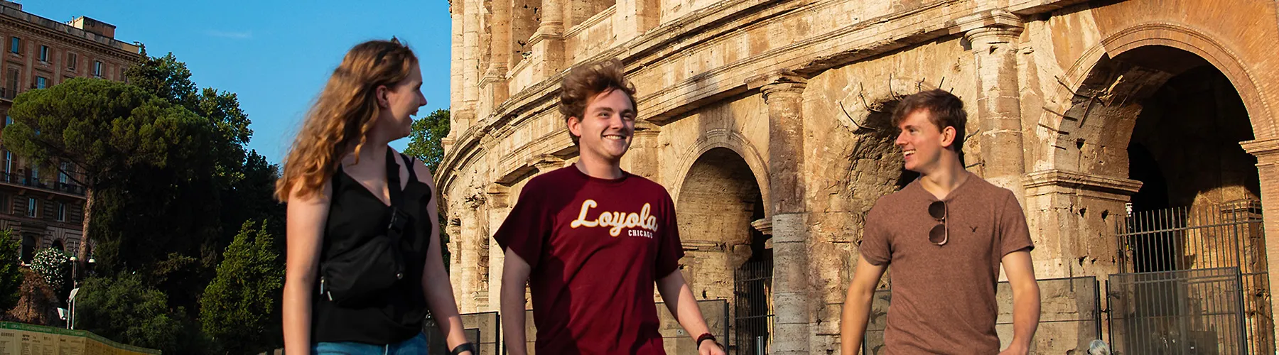 A small group of students who attend classes at the Rome Center walk together around the Coliseum in Rome.