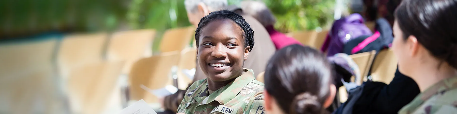 A smiling young military woman interacts with other military personnel and veterans.