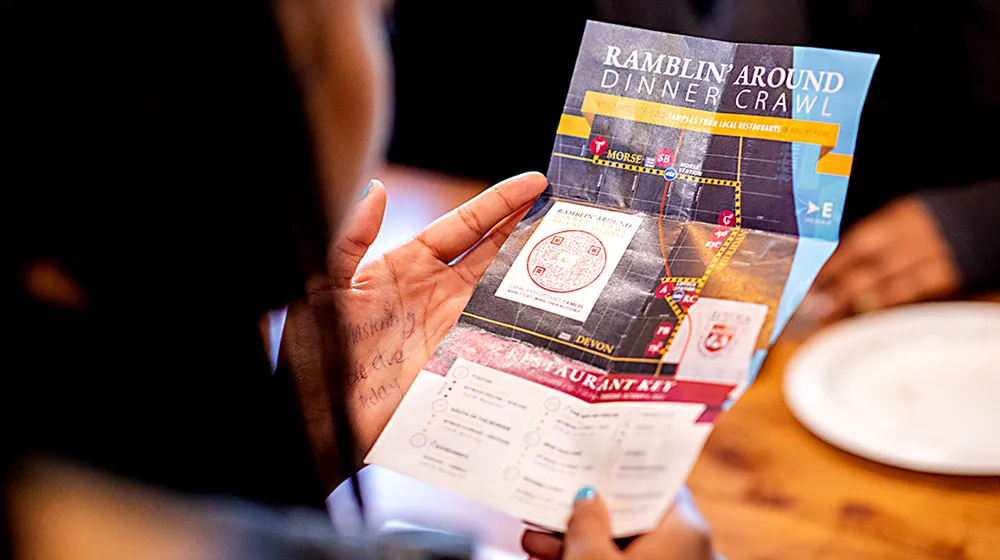 A person holds a colorful Ramblin' Around Dinner Crawl map and flyer.