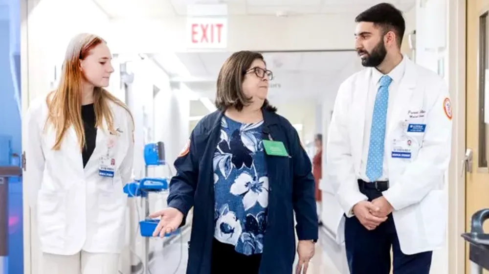 Chaplain Maria Rego-Herrera, walks along with two medical students in a bright and mostly white hallway within the Stritch School of Medicine. Chaplain Maria Rego-Herrera, walks along with two medical students in a bright and mostly white hallway within the Stritch School of Medicine.