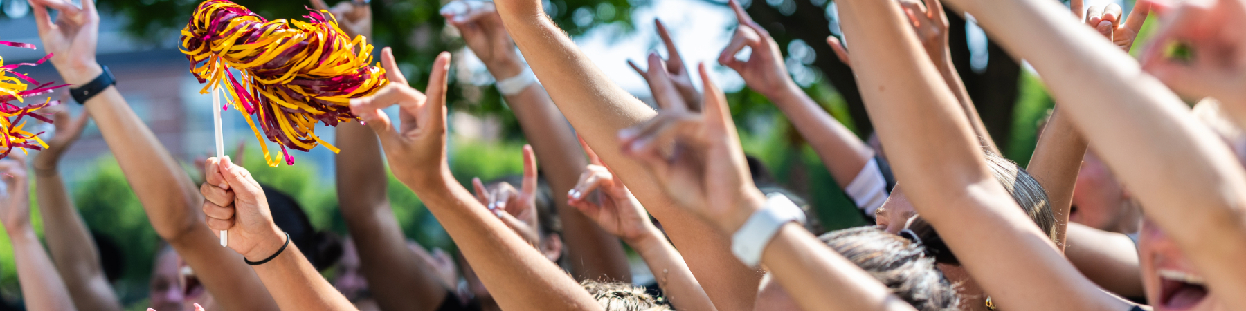 Close up image of students holding up a wolf symbol with their hands, waving pom-poms with their hands in the air.