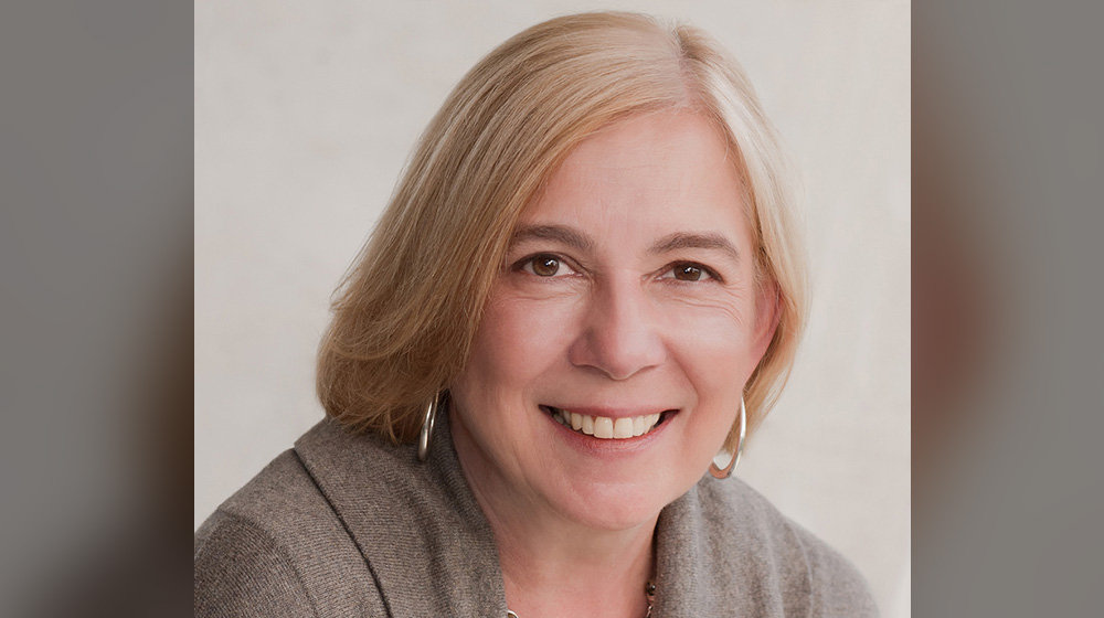 Bren Ortega Murphy smiling at the camera in a beige dress coat. Bren Ortega Murphy smiling at the camera in a beige dress coat.