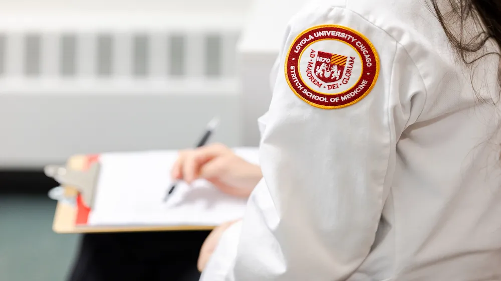 学生が書類を完了している様子。ロヨラ大学シカゴ・ストリッチ医学部のパッチが付いたホワイトコート