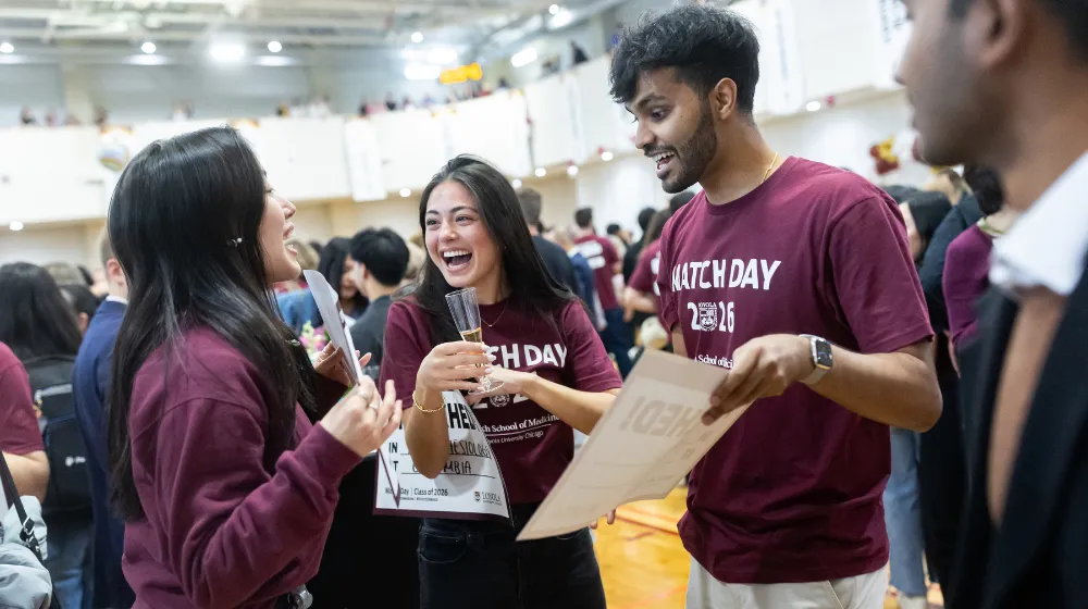 Athena Barrett pictured in center wearing maroon t-shirt and holding a champagne glass celebrates alongside two classmates
