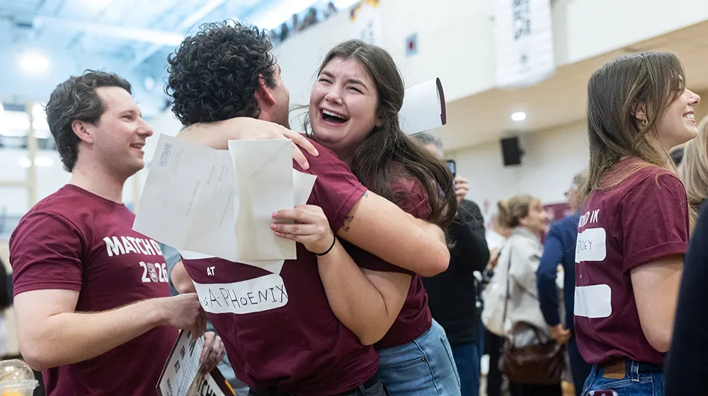 Students wearing maroon t-shirts hugs while one cries tears of joy.