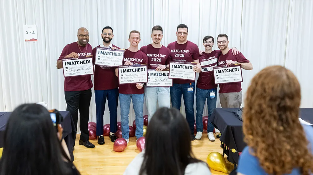 Seven students wearing maroon Match Day 2026 t-shirts and holding signs saying what specialty they matched into and where