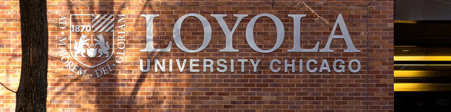 The Loyola University Chicago Logo sunlit on a brick wall of Maguire Hall on the Water Tower campus.