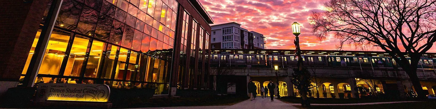 The sun sets and lights up the west sky with pink, purple, and gold, over the elevated Loyola stop on the Lake Shore campus