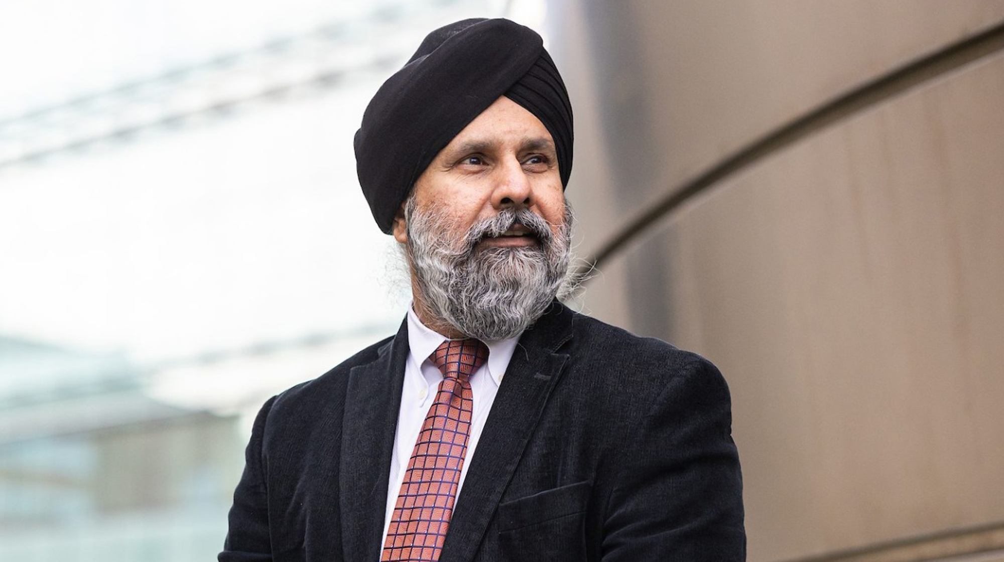 A man wearing a black turban, suit, and patterned tie, looking to the side