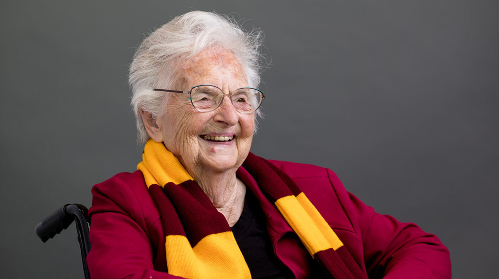 A smiling woman wearing a Loyola University Chicago scarf poses in a wheelchair