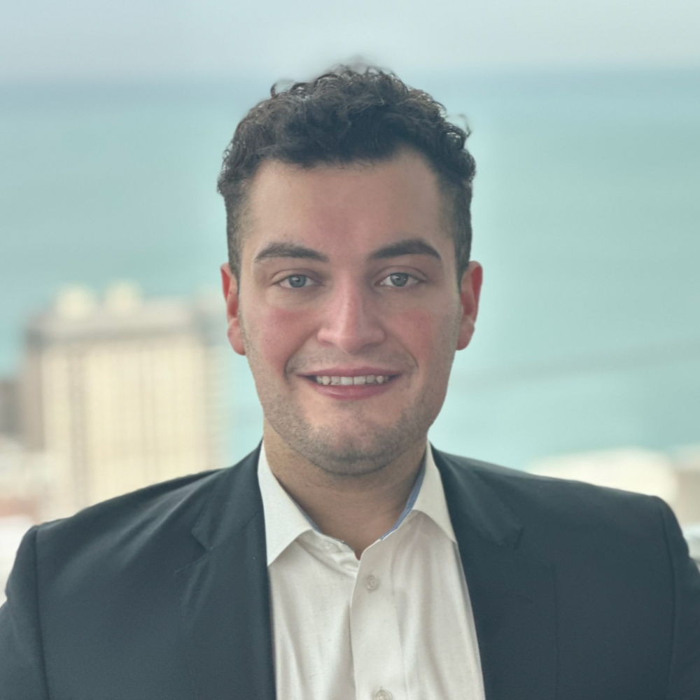 Professional headshot of a smiling man in a suit with a lakefront city skyline in the background
