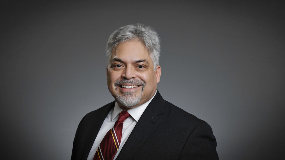 Smiling man in a suit and tie against a gray background.