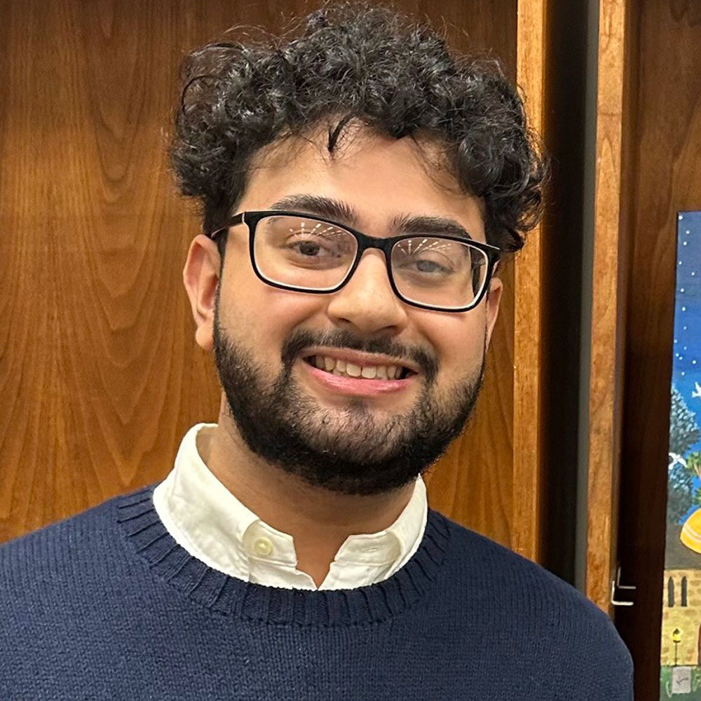 Loyola Chicago Middle East and Islamic Studies student Zayd Mushtaq. He is standing next to his winning artwork, displayed on an easel.