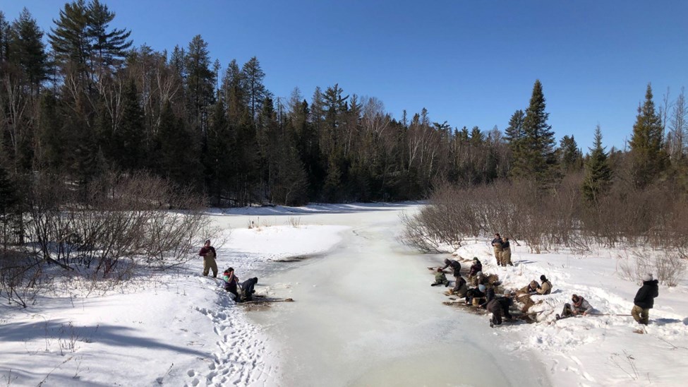 Students in Professor Berg’s Insects class collect aquatic insect samples along a partially frozen river in winter, surrounded by snow-covered banks a