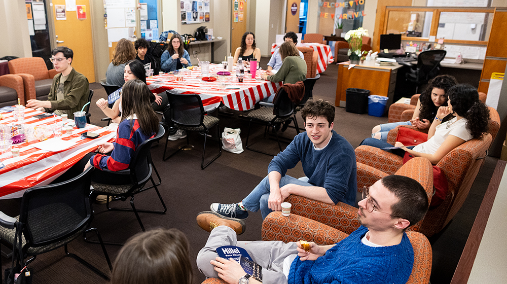 Students gathered in a campus lounge for a Jewish community event, seated at tables and talking
