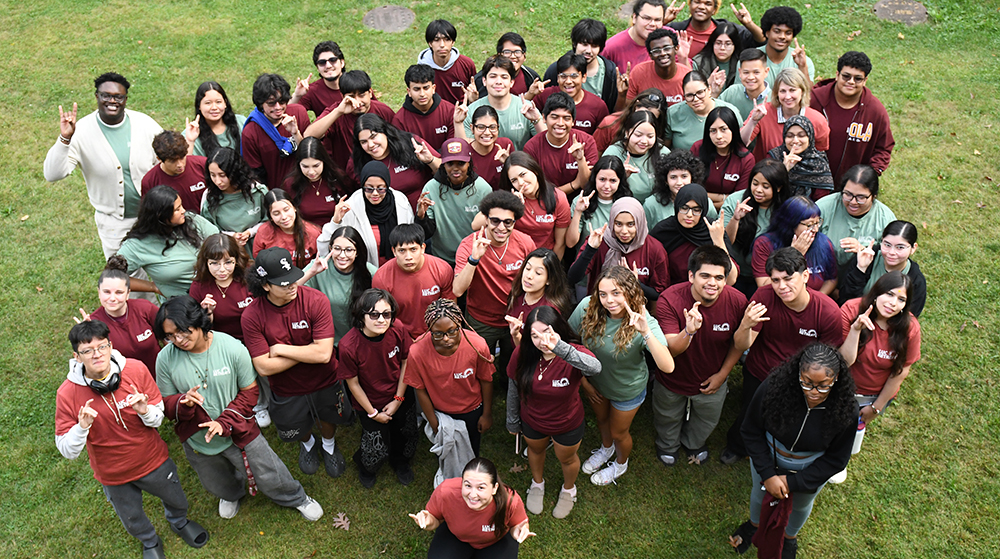 Large group of students in matching shirts gathered on a lawn, posing and smiling for a photo.