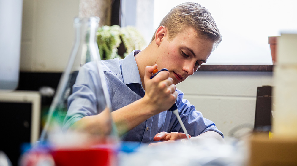 Student using a pipette while working at a laboratory bench.