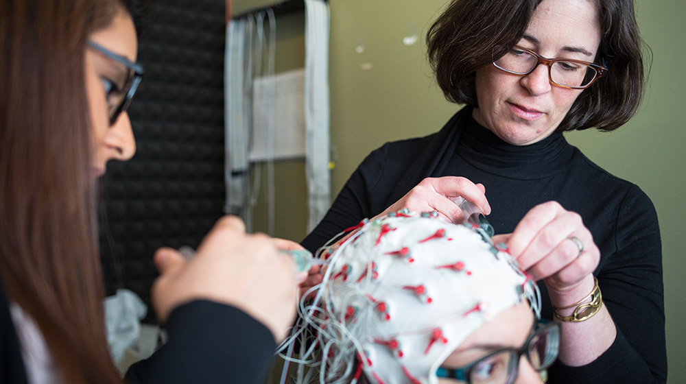 Researchers adjust EEG cap on participant during brain activity experiment.