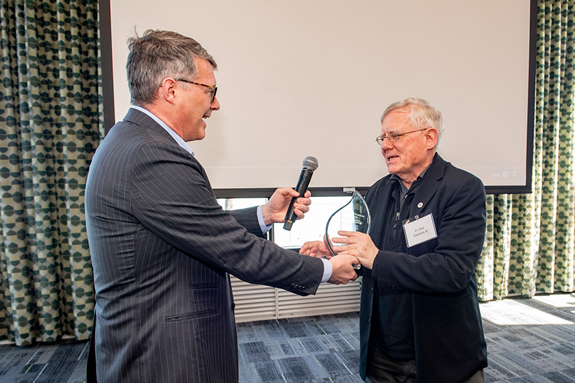 Man presenting an award to another man while holding a microphone in a conference room