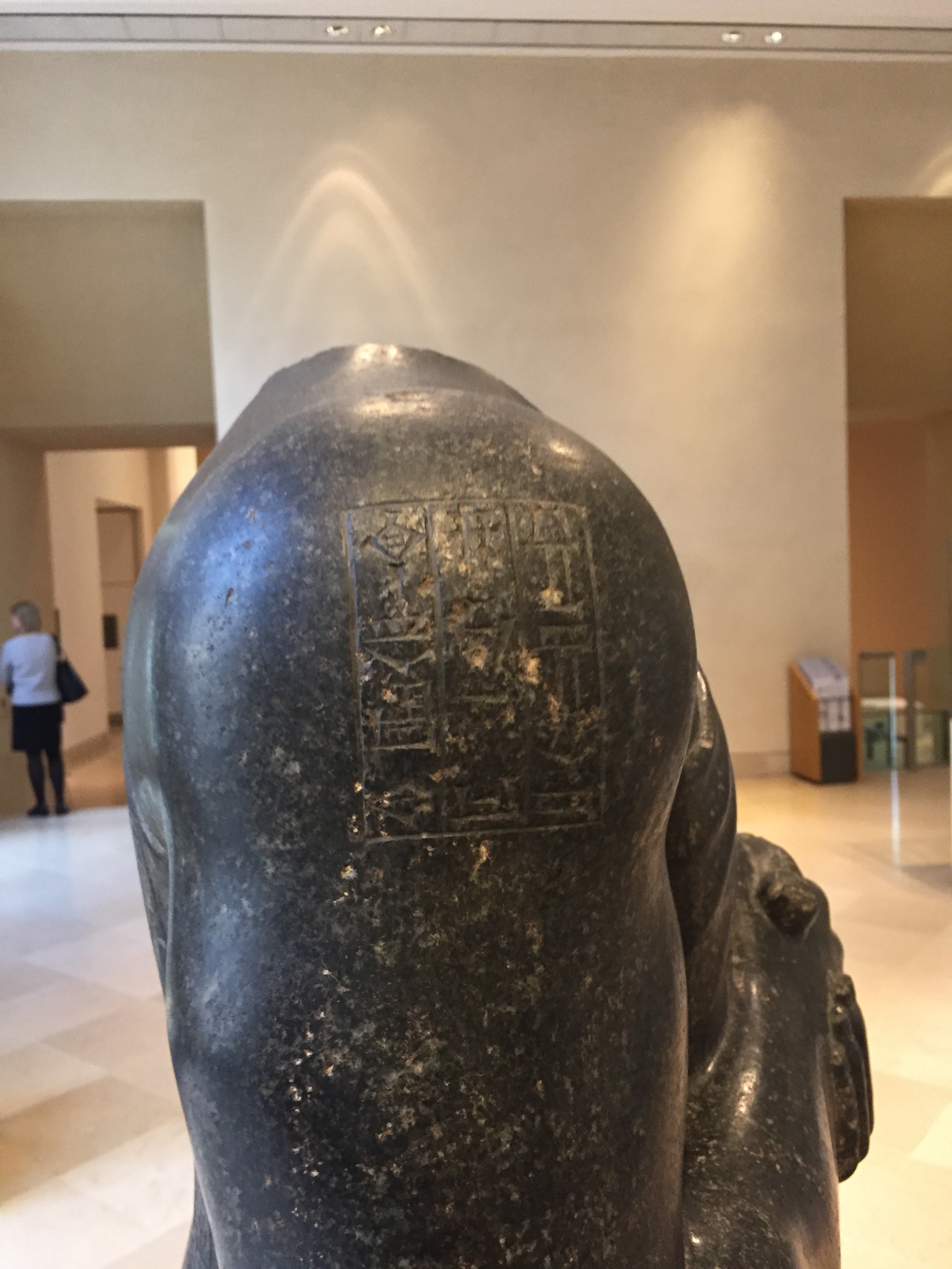 Back of a stone statue head with carved hieroglyphs, displayed in a museum gallery