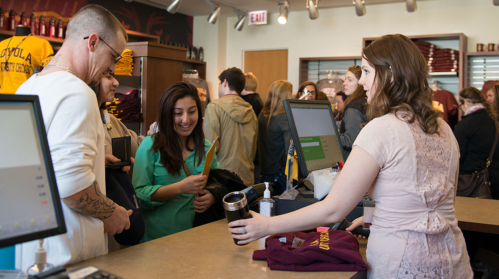 Students purchasing items at a campus bookstore counter, with Loyola apparel visible in the background.